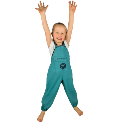A toddler wearing green grubberalls with a logo on the front, designed for waterproof and outdoor play.
