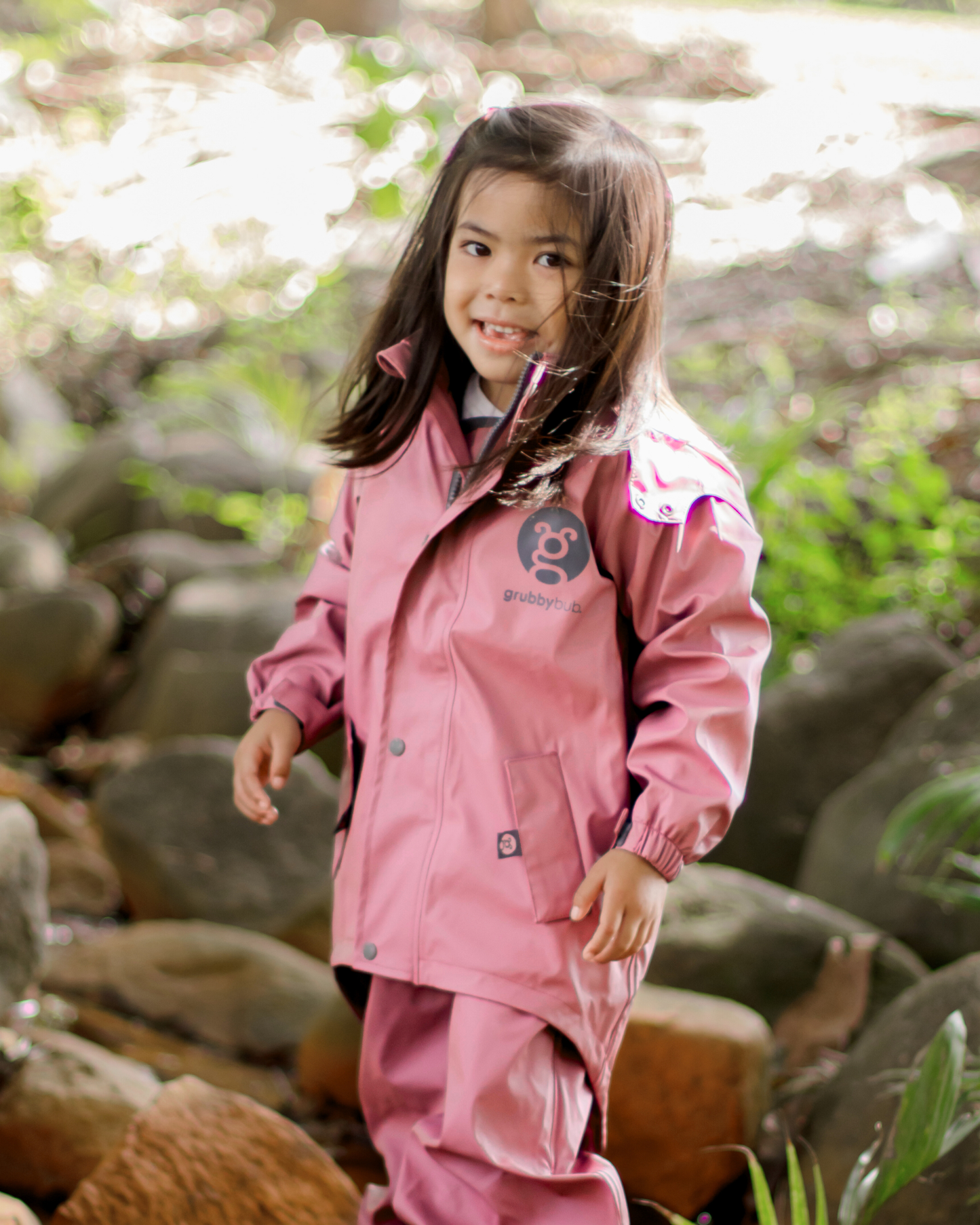 Child in pink waterproof rain jacket with mud guard walking through nature, kids all weather jacket