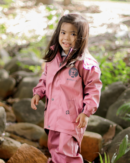 Child in pink waterproof rain jacket with mud guard walking through nature, kids all weather jacket