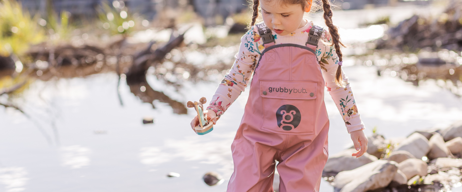 Child exploring creek during outdoor play wearing waterproof overalls, ideal for forest school and nature adventures