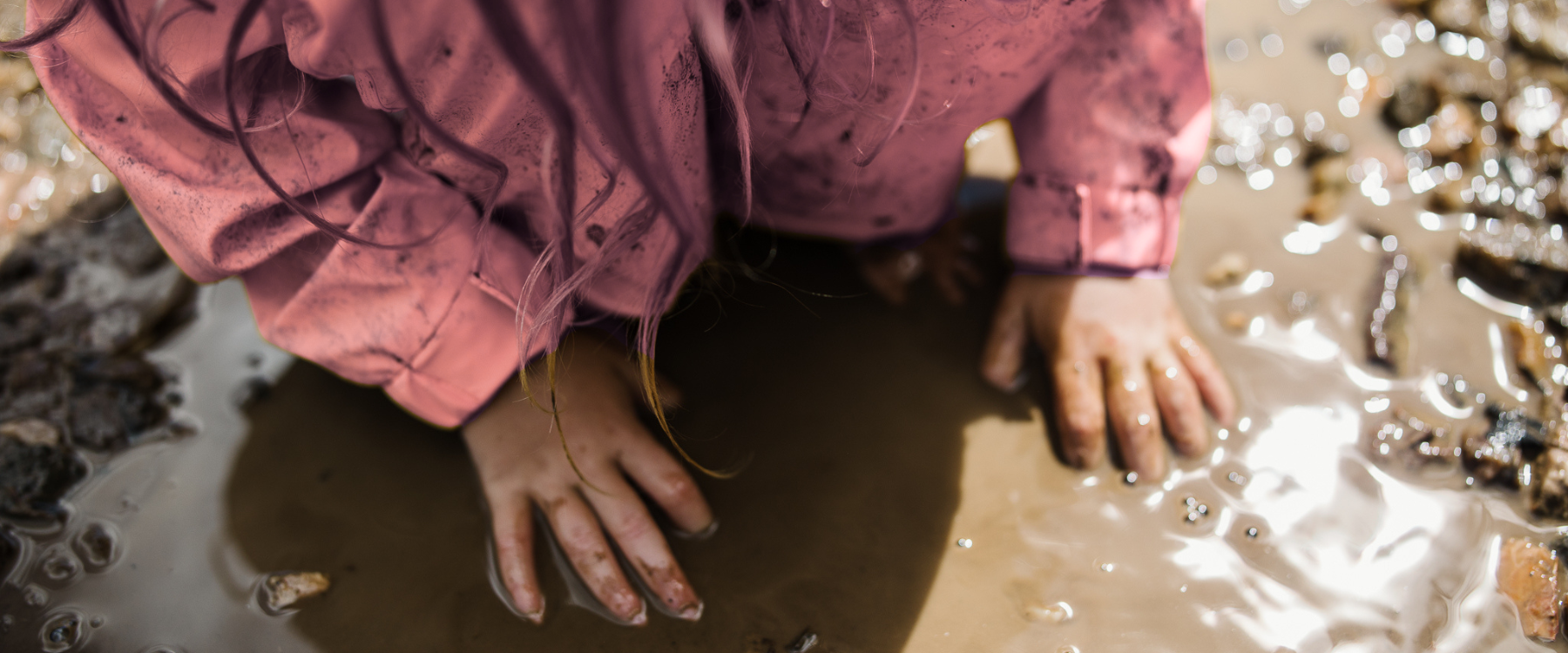 Child engaging in muddy sensory play during forest school, hands in water and mud during outdoor learning