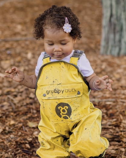Child wearing yellow 'grubby bub' waterproof rain overalls in a forest setting