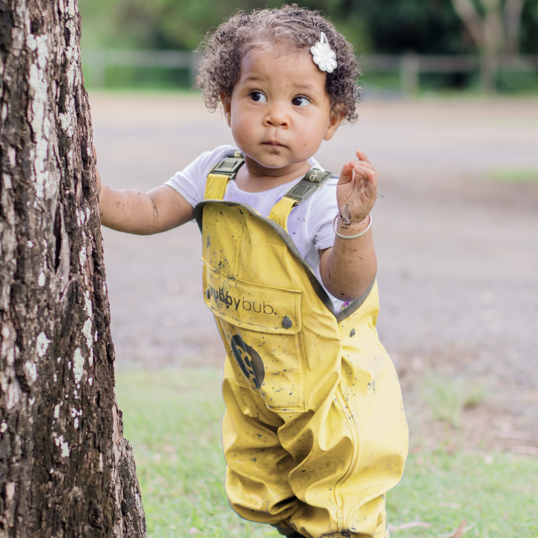 Child standing by tree during outdoor play, wearing waterproof overalls for forest school and nature exploration