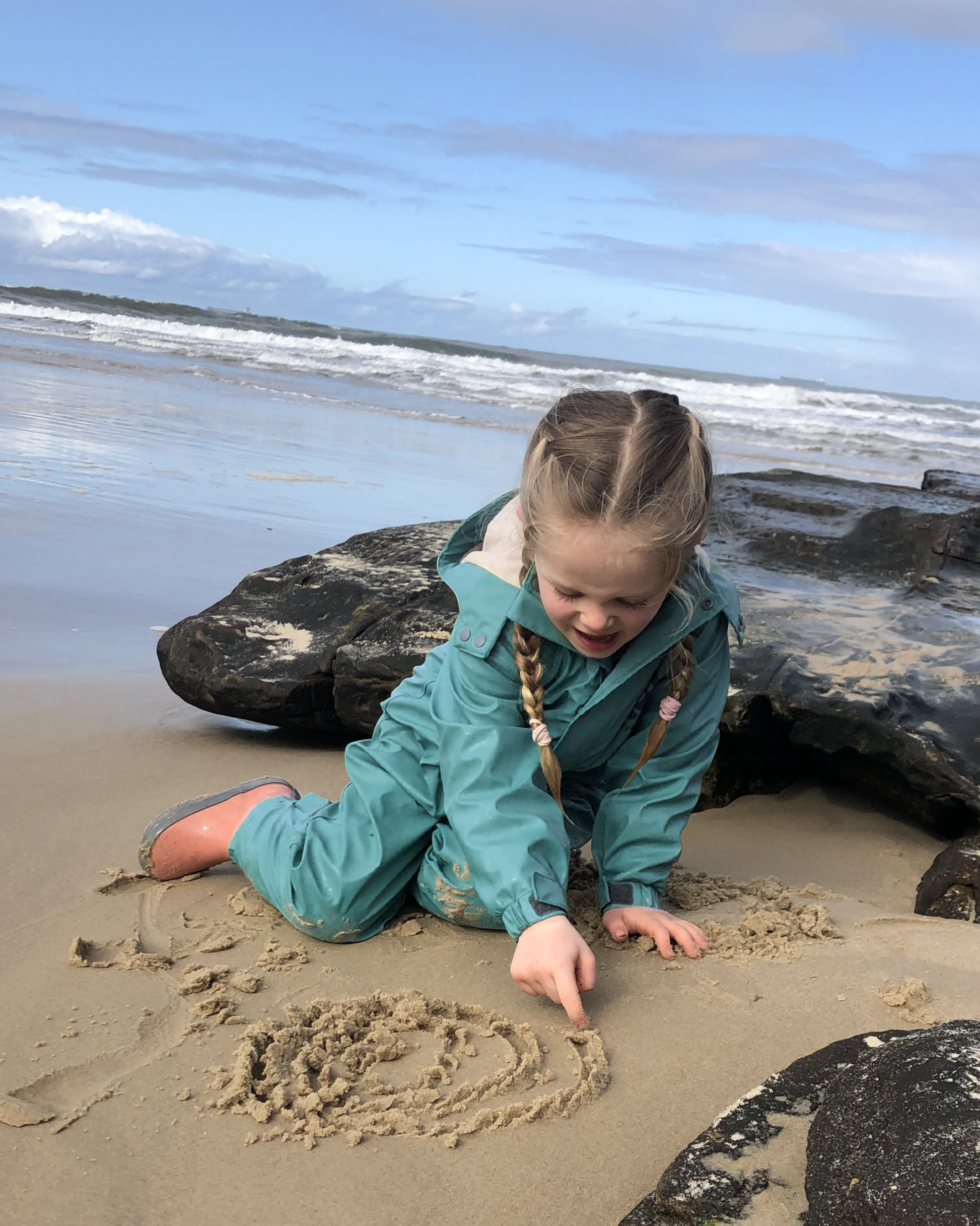Child in waterproof rain suit playing on beach in winter, kids outdoor all weather suit for sand and water play