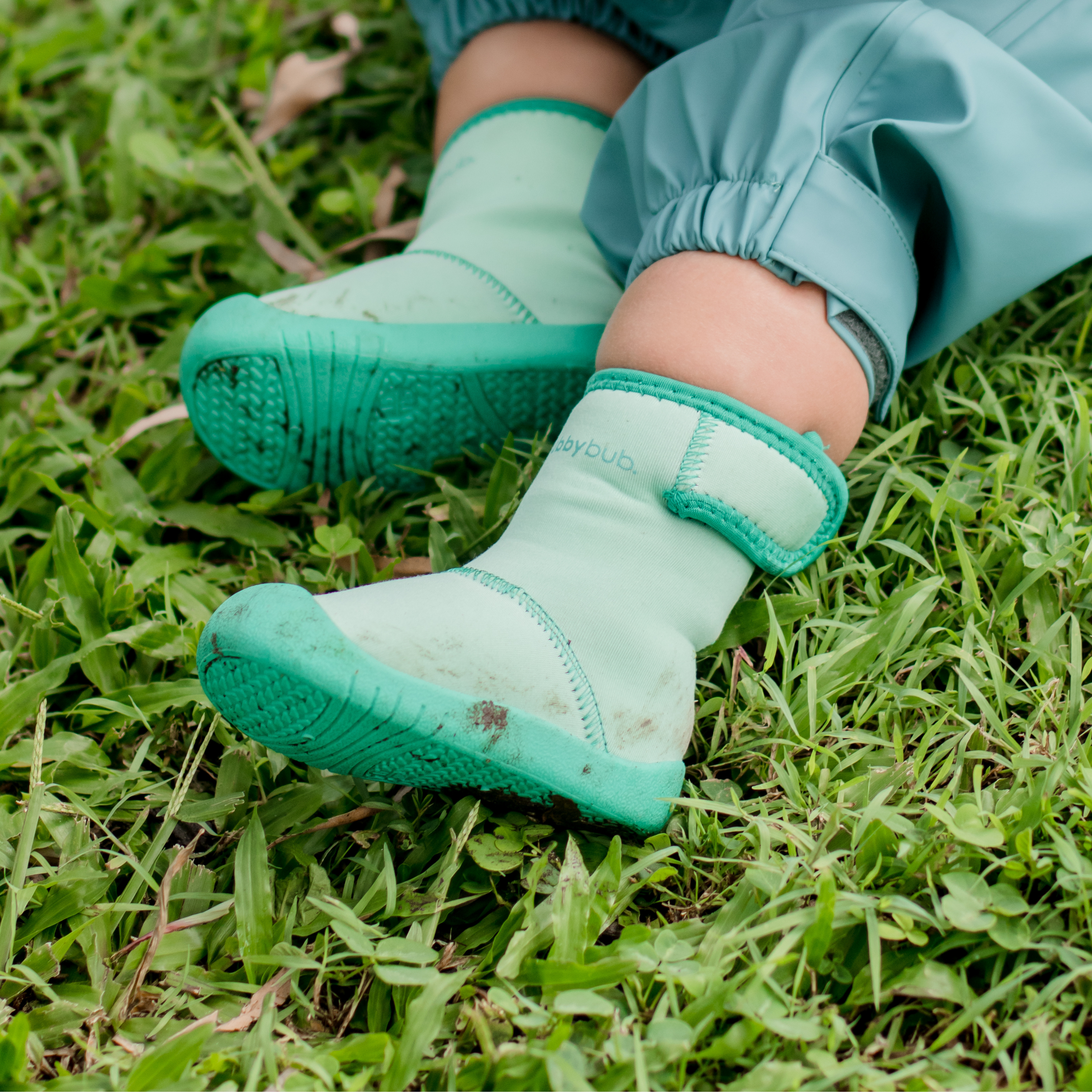 Toddler feet in green Wee Wellies boots resting on grass showing soft flexible soles for outdoor play